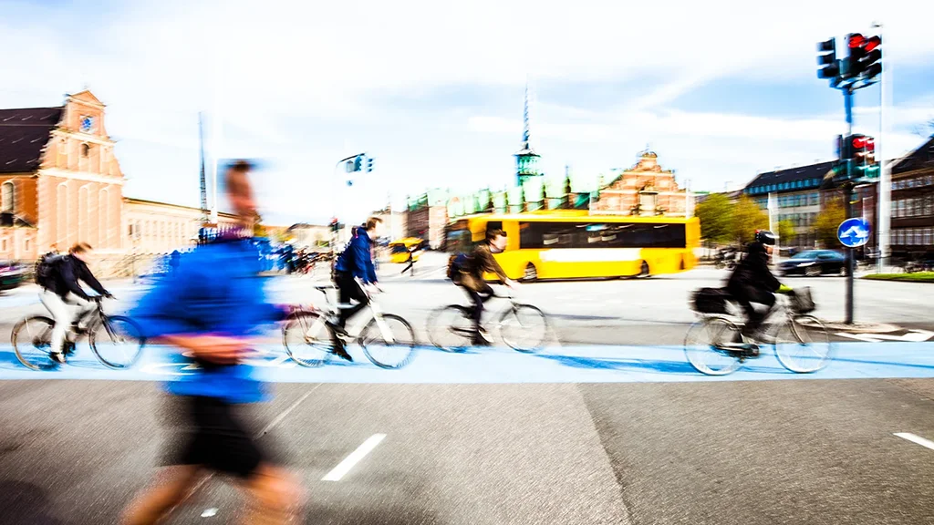 Ihmisiä lenkkeilee ja pyöräilee kaupungin keskustassa, taustalla linja-auto